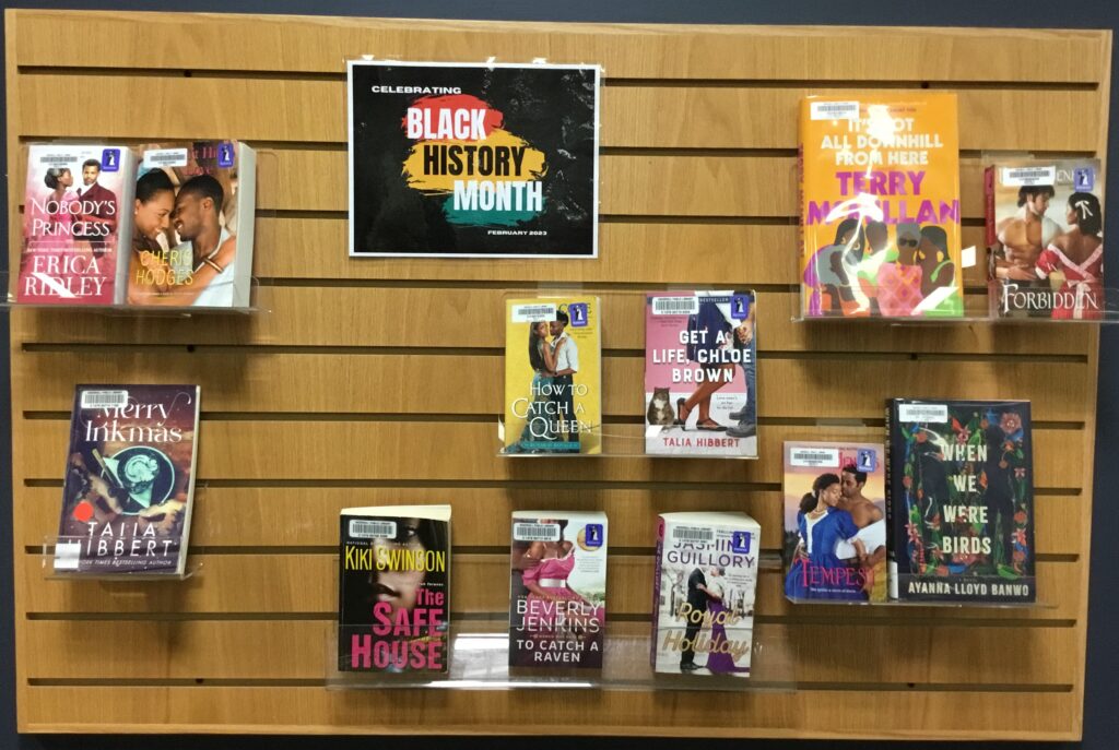 Plastic shelves hanging on wall containing books. Sign at top states "Celebrating Black History Month: February 2023."