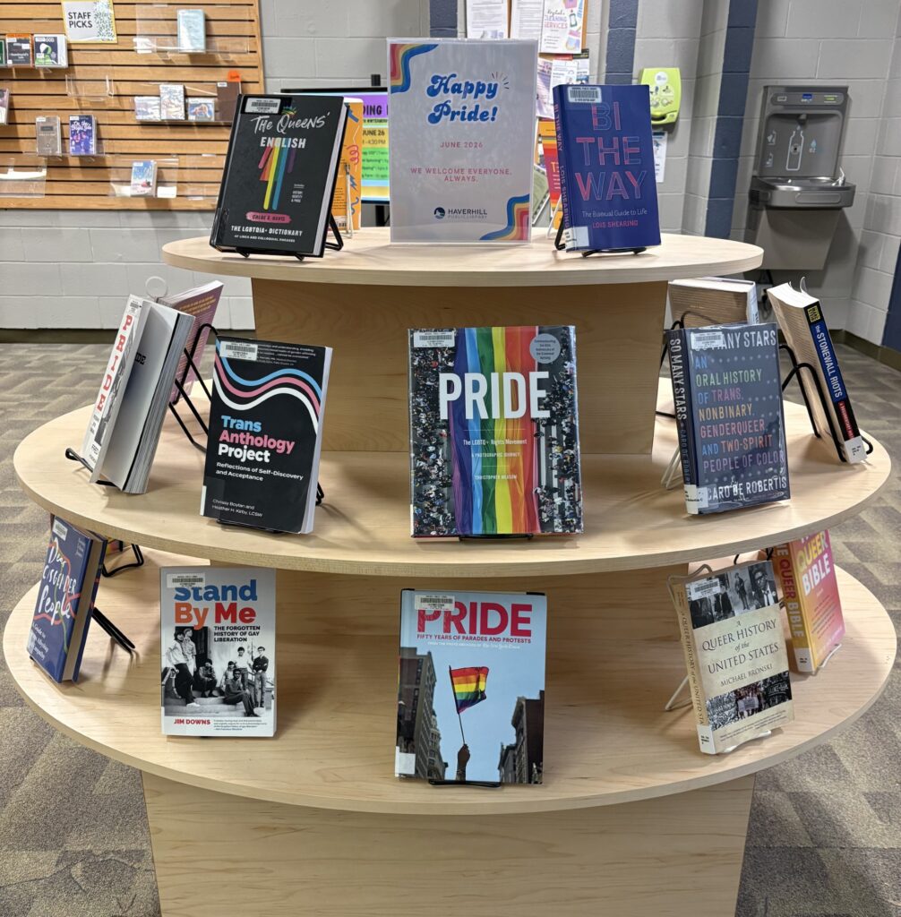 Books on a set of round display shelves with a sign at the top that says "Happy Pride! June 2026. We welcome everyone, always." The books relate to LGBTQIA+ communities and histories.