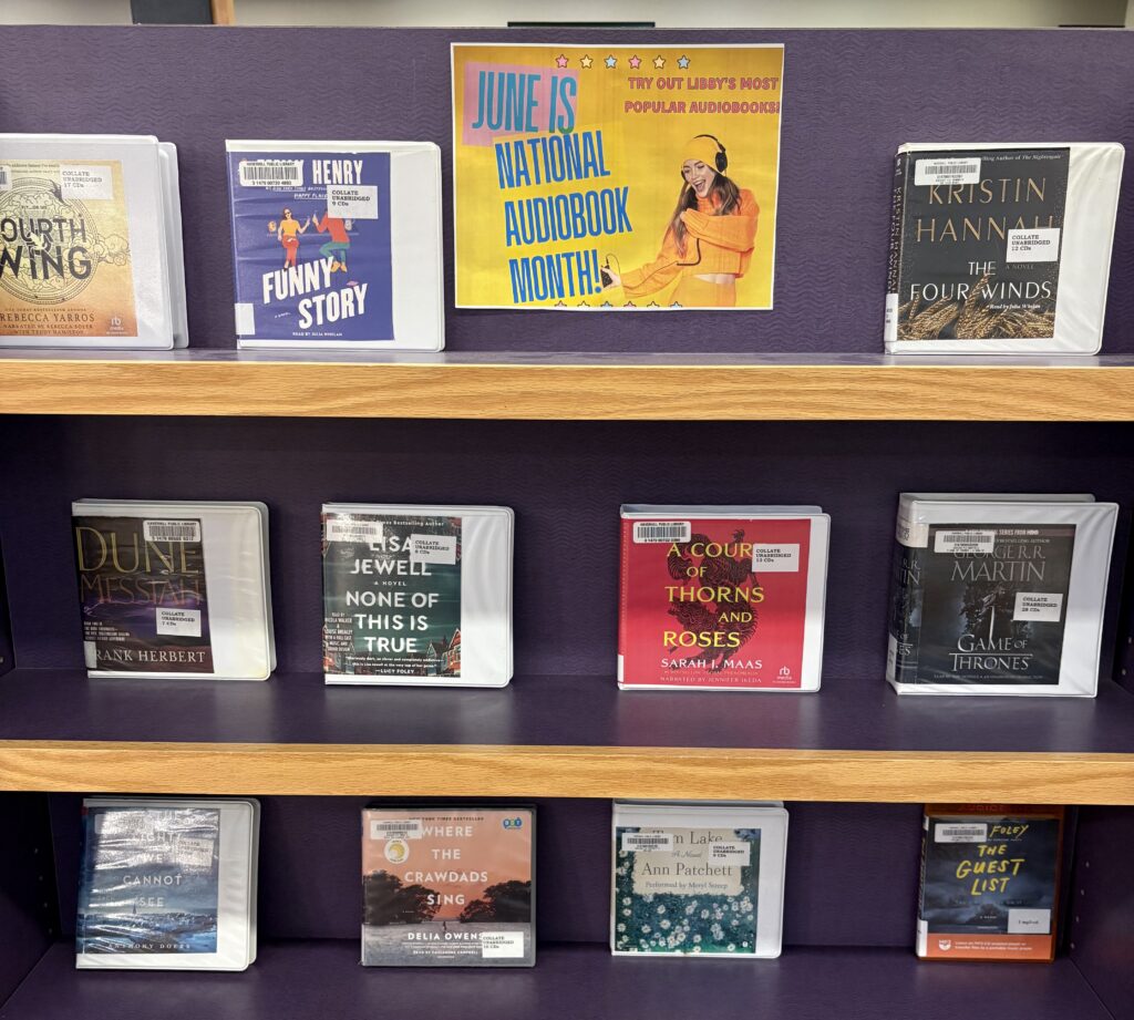 Audiobook CDs in cases on a display shelf, with a sign at the top that says "June is National Audiobook Month! Try out Libby's most popular audiobooks!"